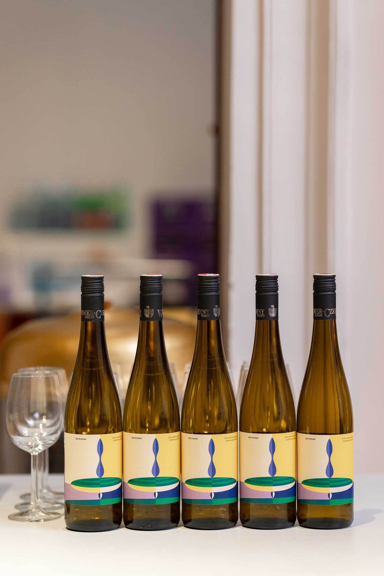 5 Weinflaschen nebeneinander auf einem Tisch. Auf dem Etikett ist ein Kreisel.