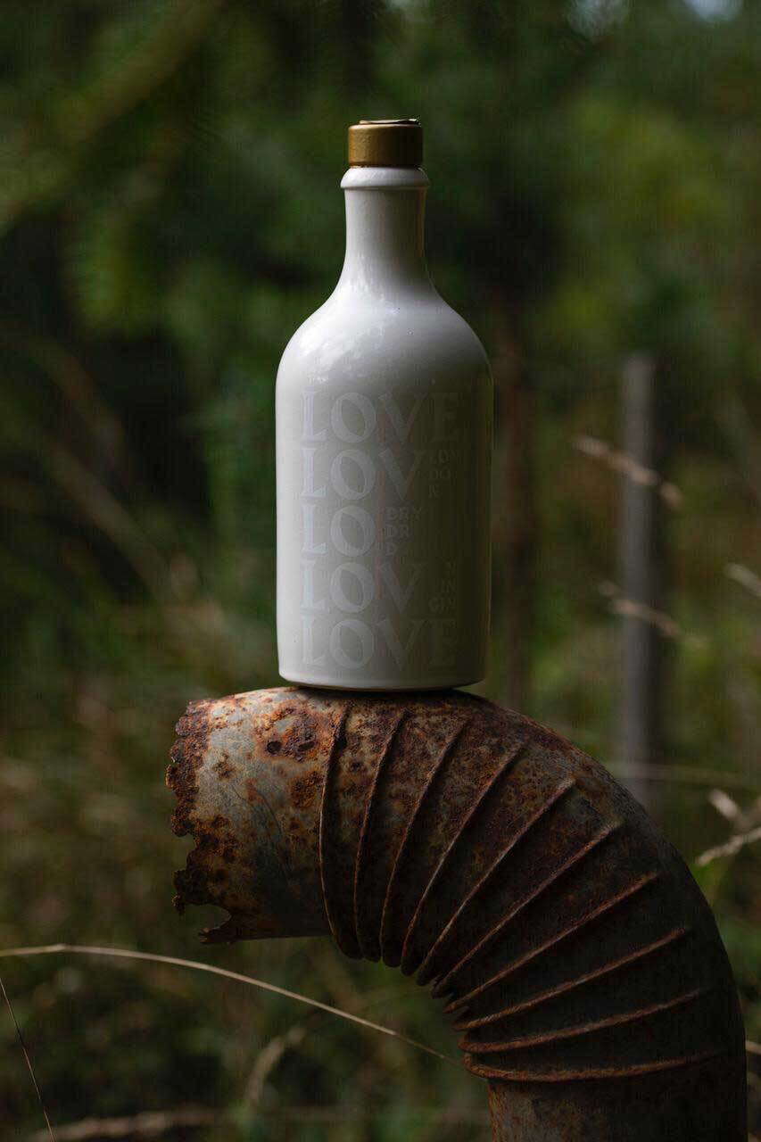 Off-white Gin Flasche mit weißem Aufdruck vor Wald, auf einem rostigen Rohr.