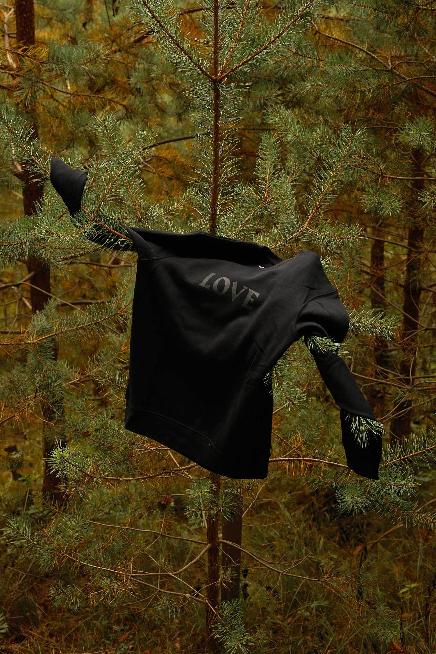 Ein schwarzer Pullover mit dem schwarzen Aufdruck "LOVE" hängt in einem Nadelbaum.