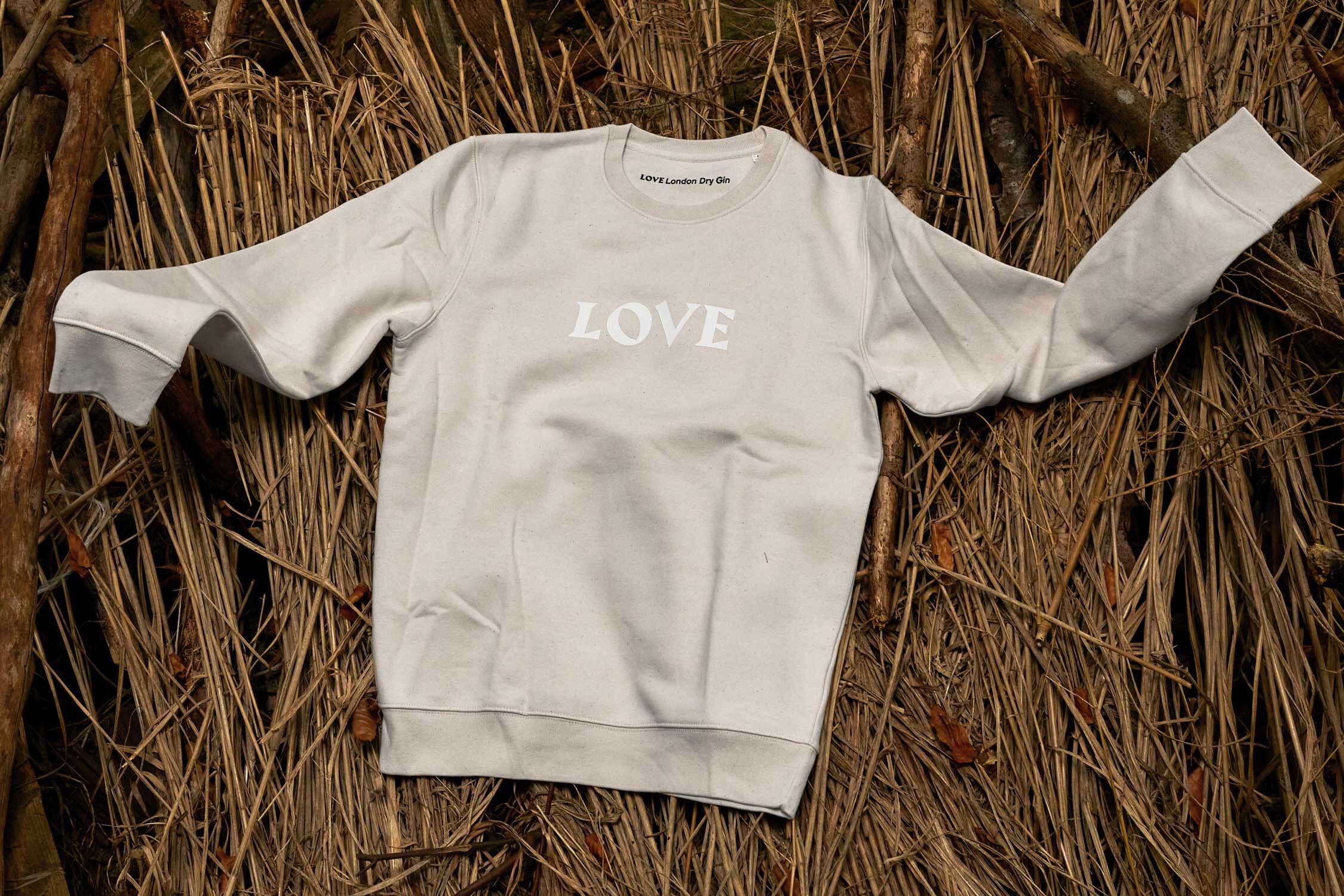 Ein beiger Pullover mit dem weißem Aufdruck "LOVE" liegt auf trockenen Gräsern.