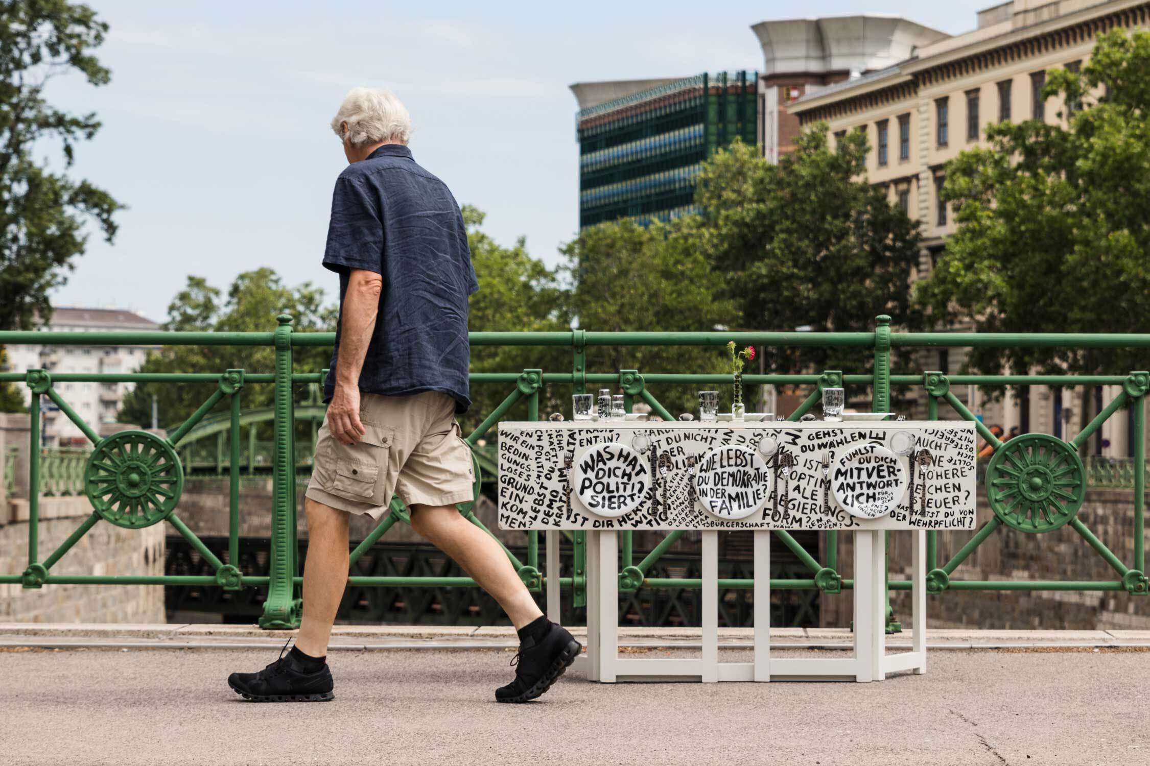 Der zusammengeklappte Tisch steht auf einer Brücke des Wienflusses, ein Mann geht vorbei mit Blick auf den Tisch.