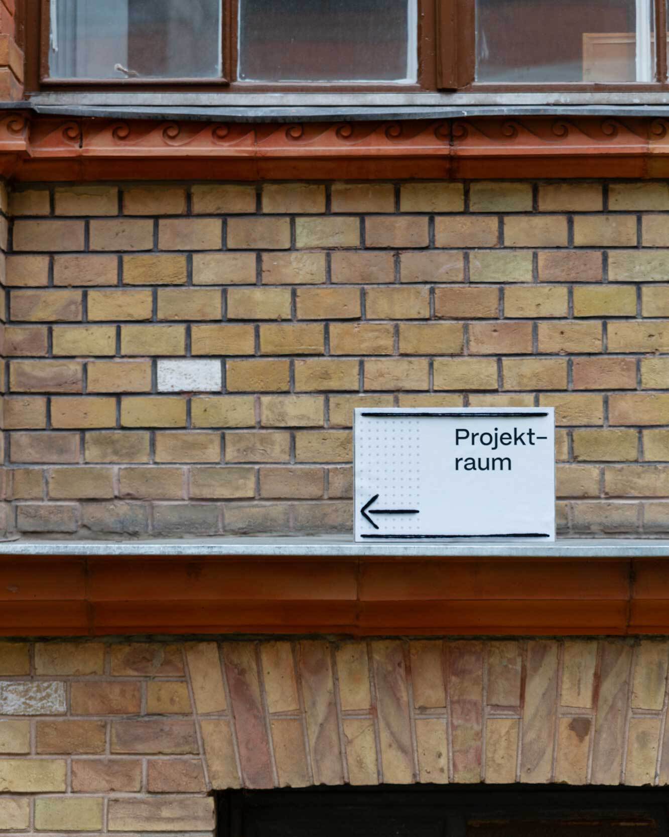 Ein Schild mit Pfeil nach links steht auf dem Vorsprung vor einer Backsteinwand.