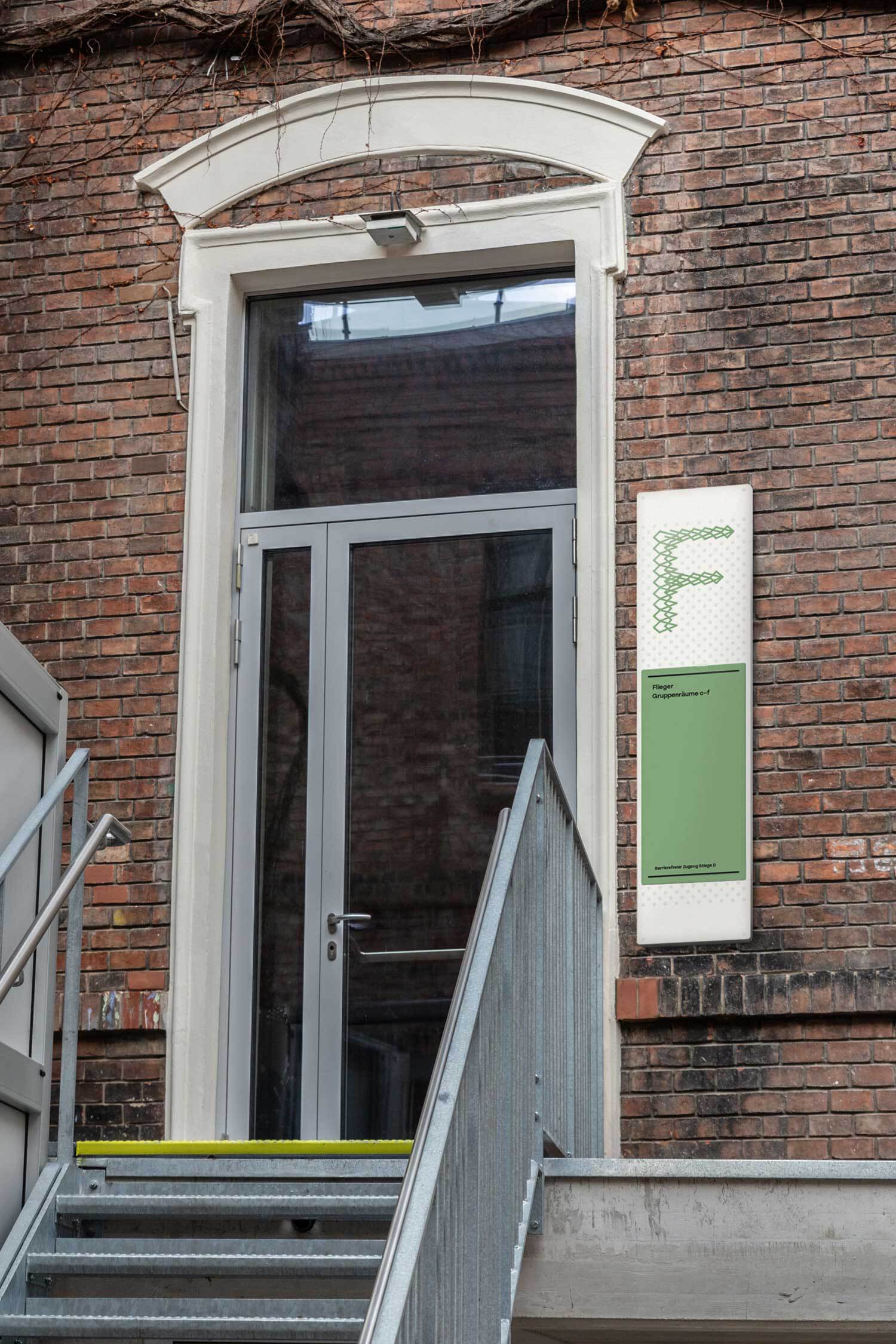 Stiegenaufgang F, Beschriftung durch ein Panel an einer Backsteinwand.
