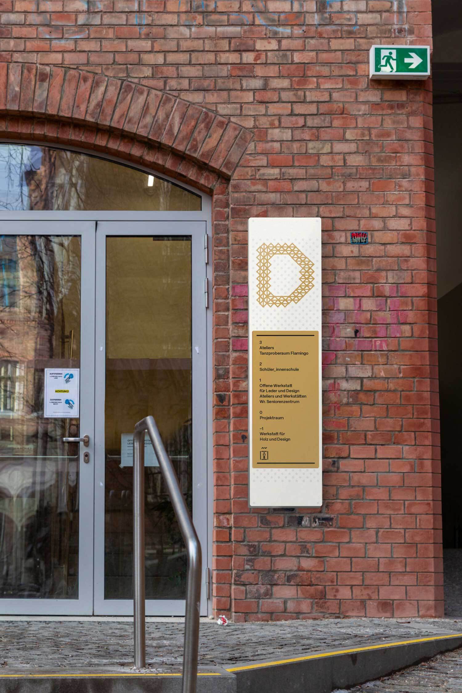 Stiegenaufgang D, Beschriftung durch ein Panel an einer Backsteinwand.